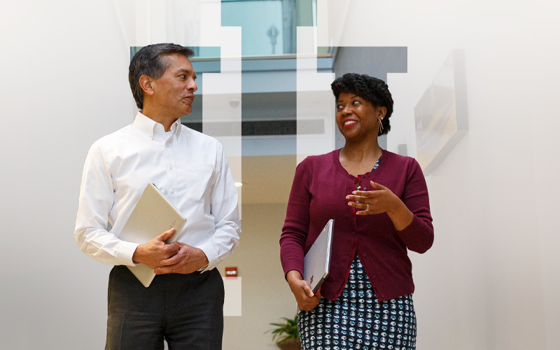 Two colleagues in professional attire walk down a hallway