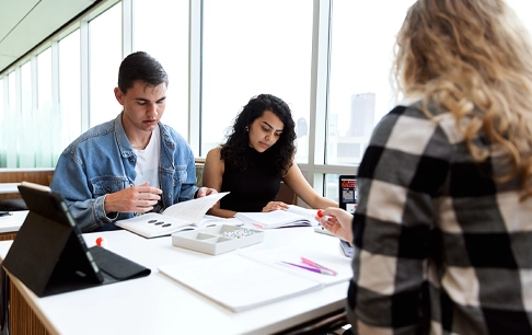 Three people sit around a large table covered in books and papers.