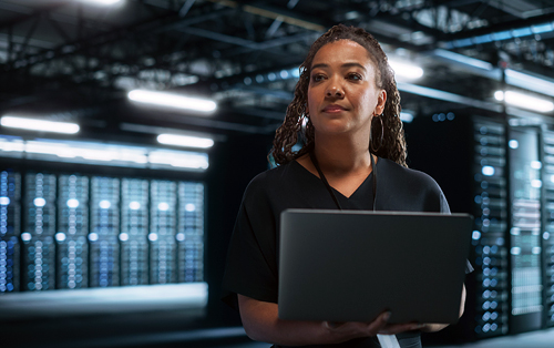A woman with a laptop standing in a data center.