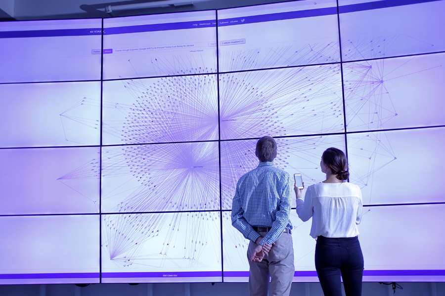 Two people stand in front of a wall of screens.