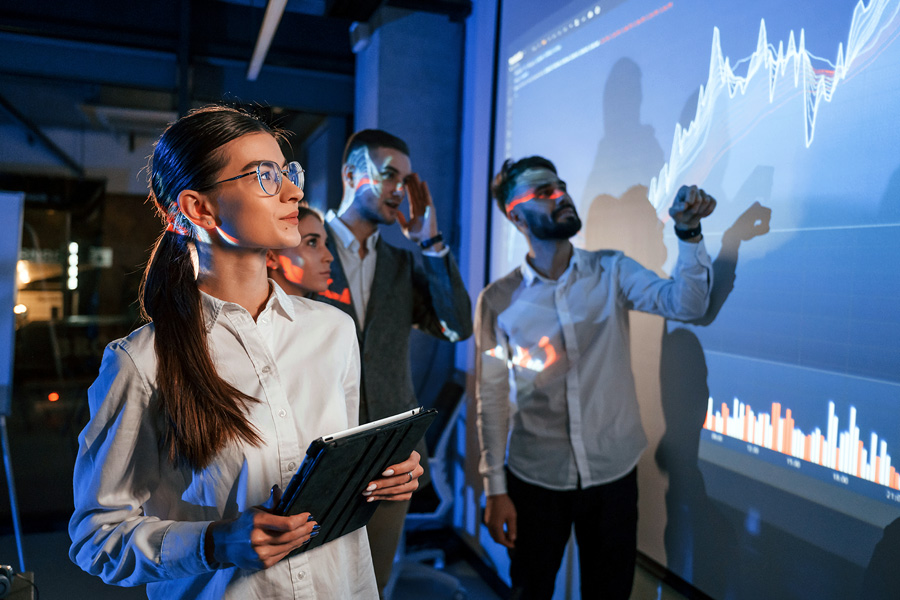 A group of people look at a large projected screen of graphs.