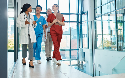 A group of four people, two wearing scrubs and two wearing doctor coats, walking down a hallway