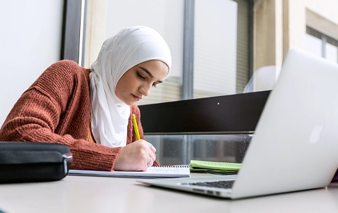 A woman writes in a notebook at her desk.