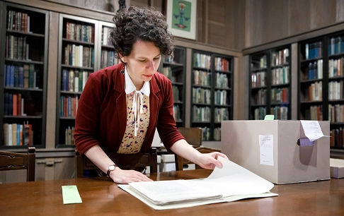 A woman looks through a historic document in an archive.