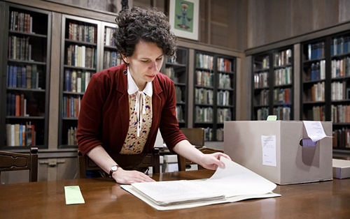 A woman looks through a historic document in an archive.