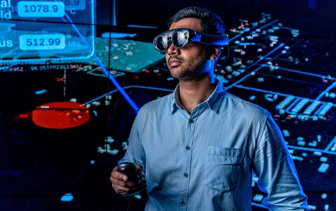 A man wearing VR goggles stands in front of a screen with data.