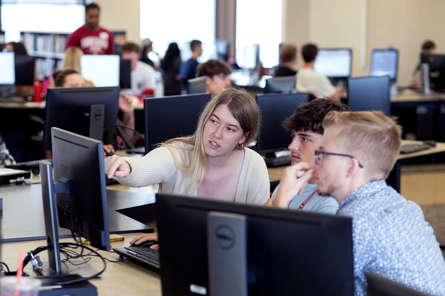 An instructor shows students something on a computer screen in a lab