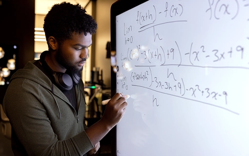 A young man works through a math problem on a digital whiteboard.