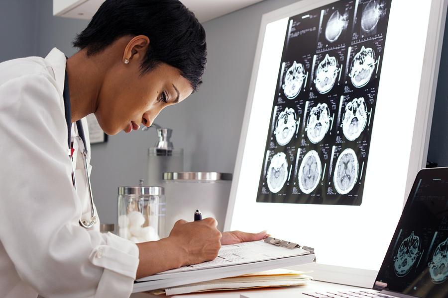 A doctor takes notes on a clipboard while looking at scans of the brain.