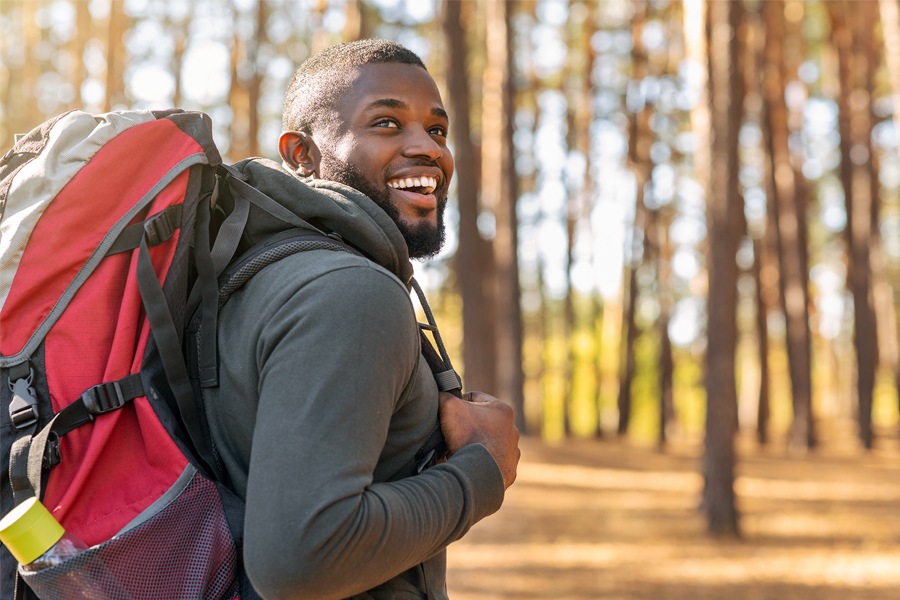 A man wearing a backpack smiles over his shoulder while walking in the woods.