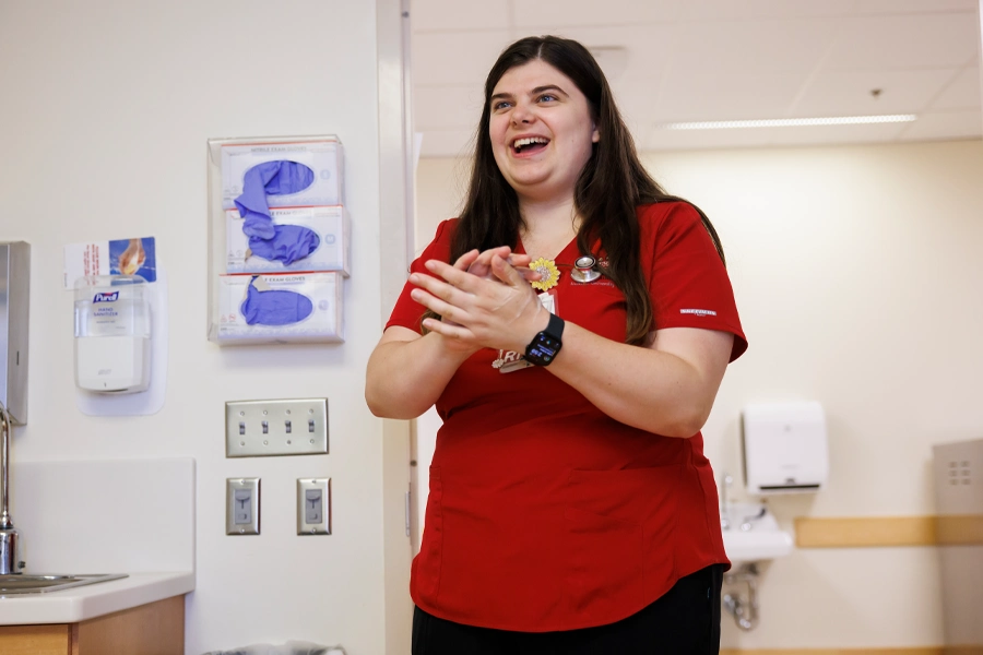 A woman in scrubs washes her hands while entering a room.