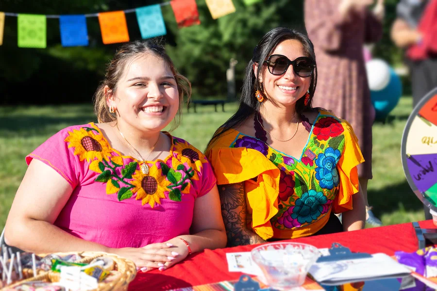 Two woman smile while seated at a booth they manage for a Hispanic Heritage event